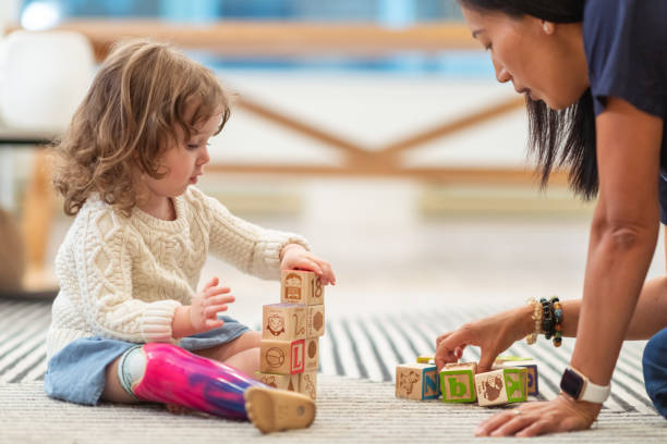 A young girl sits on the floor and plays blocks with the child life specialist.