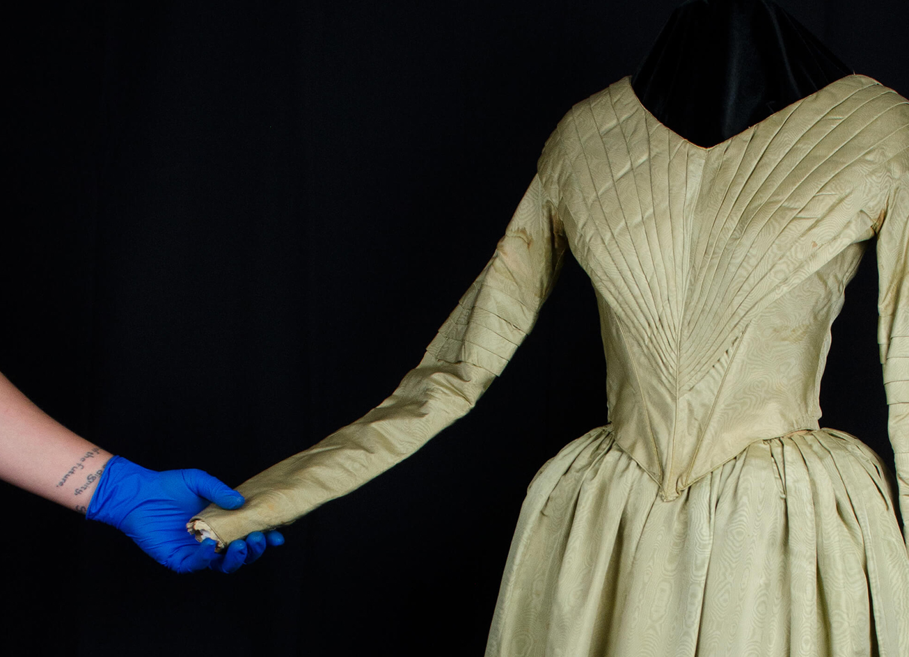 Photographer holding the arm of a green 1840s dress while it is on a mannequin