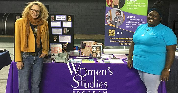 two women stand in front of a table with promotional materials