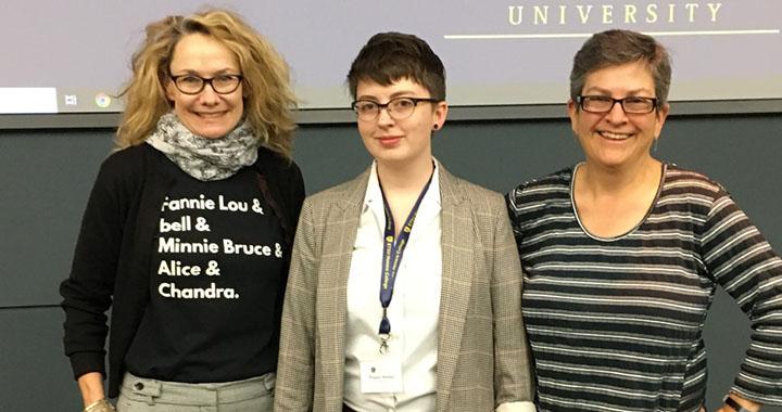 three people stand in front of a presentation screen