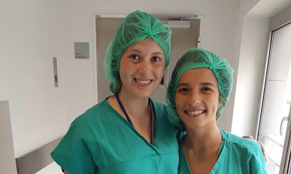 Two students pose together in scrubs and hair nets.