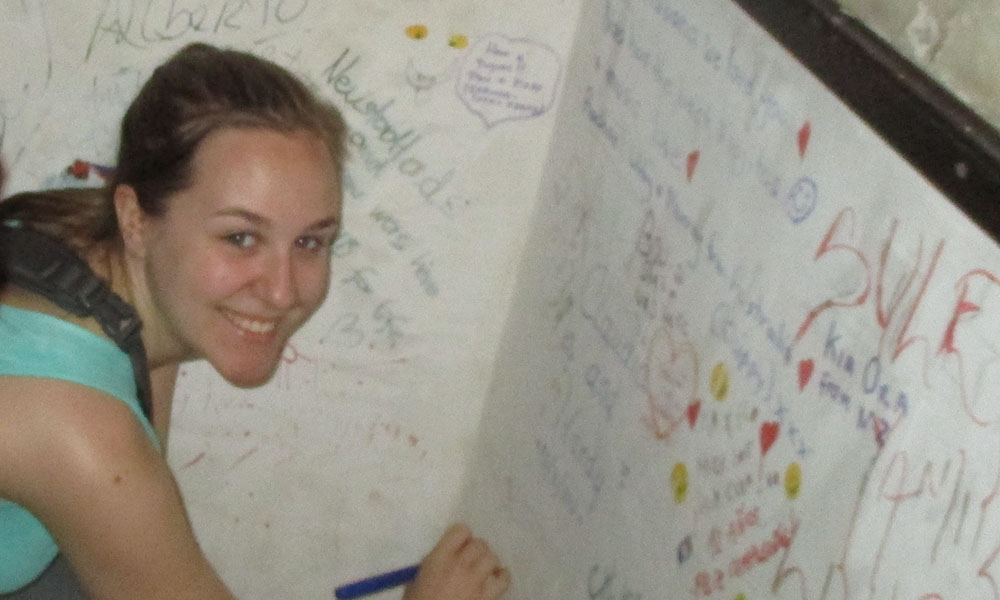 A white female college student signs her a wall of graffiti signed by many before her.