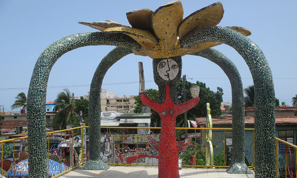 A surreal/abstract mosaic sculpture of a woman in red, with a cubist face and a flower sprouting out of her head.