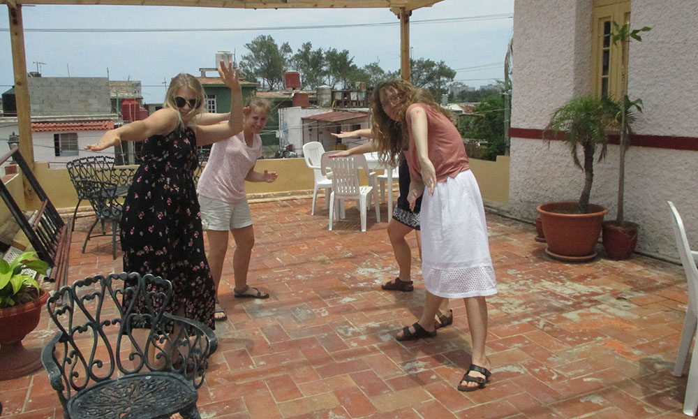 Four, blond women dancing on a patio, stop and pose looking at the camera.