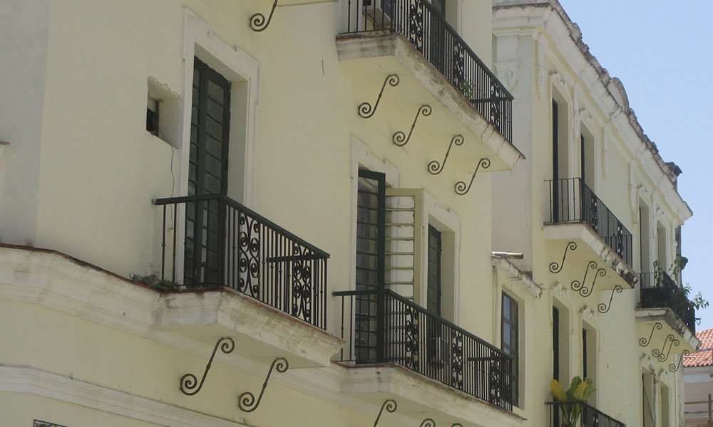 A colonial style building with balconies supported and framed by scroll-worked iron.