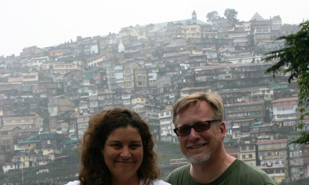 Dr. Schrift and "K" pose in front of a cramped, sloping hillside city.