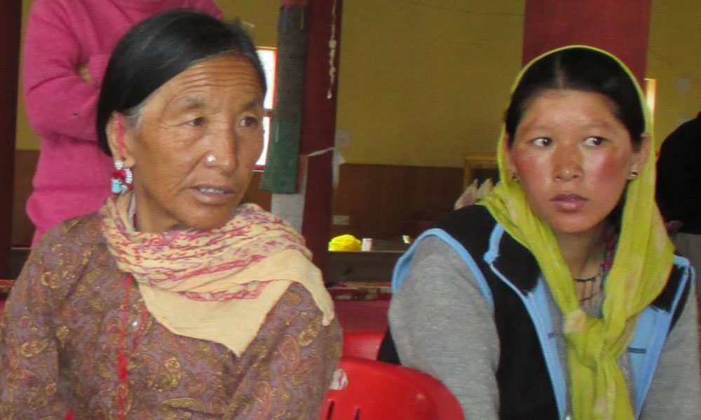 Two Himalayan women in scarves listen to someone off frame.