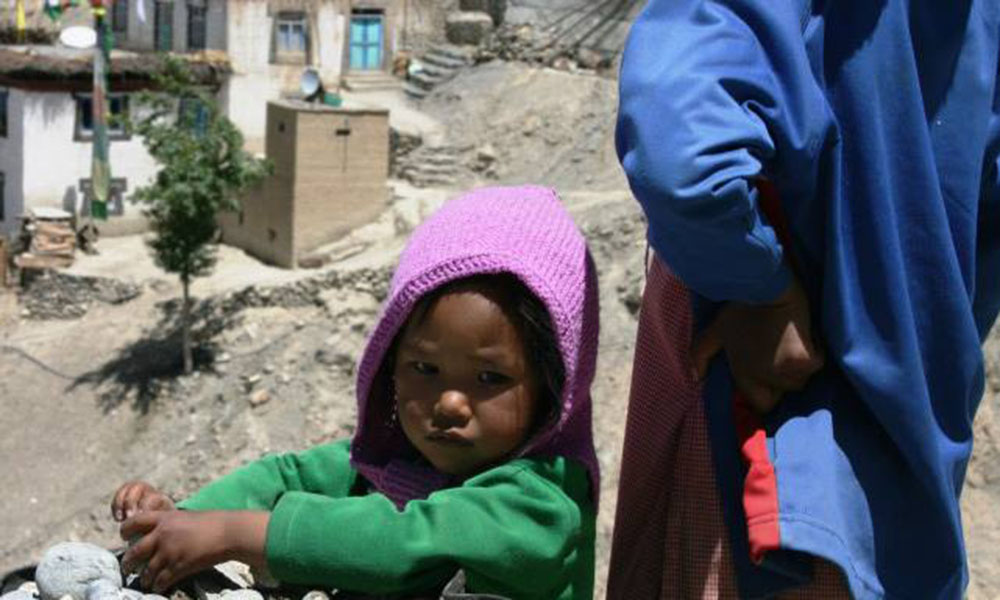 A young Himalayan child holds a rock while their parent looks out over the neighborhood beyond.