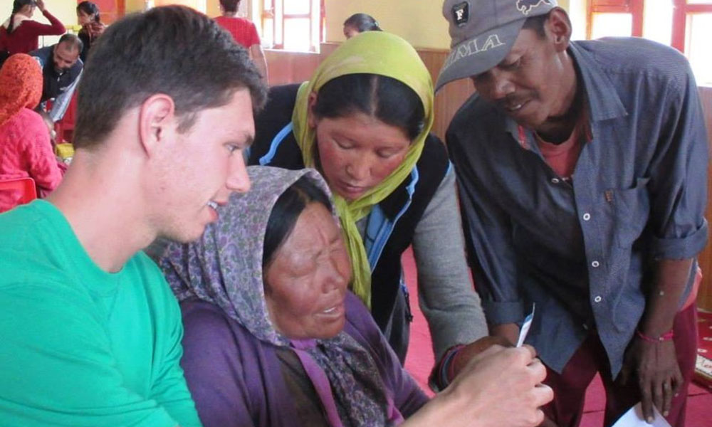 A young white man looks at a photo with three locals, two women in headscarves and a man in a ballcap.