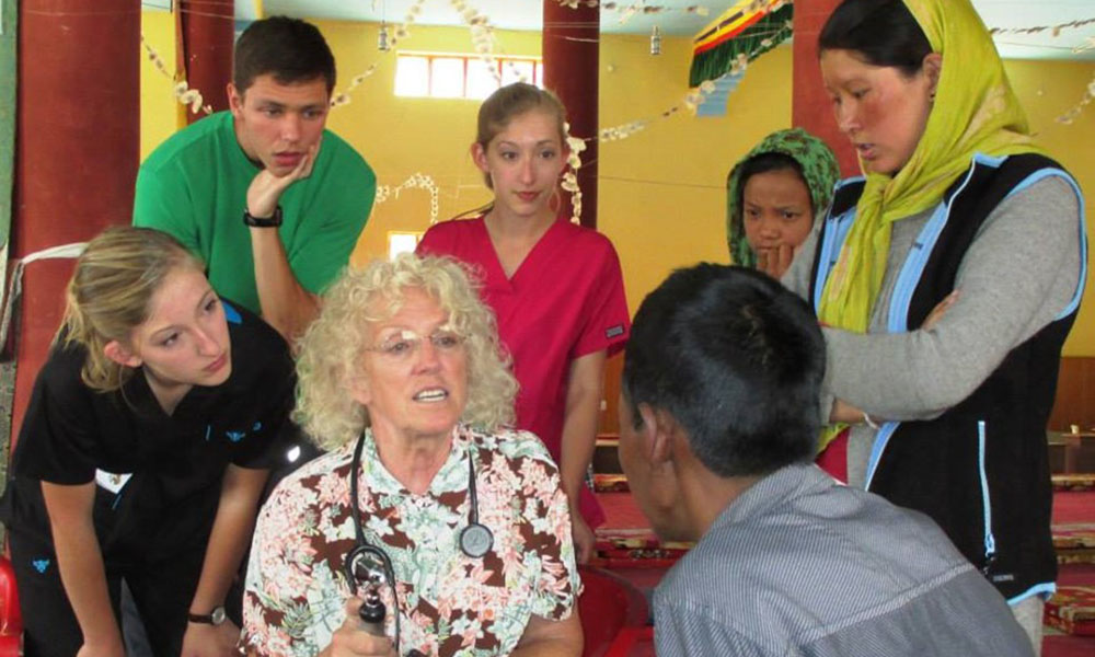 A mixture of students and locals listen/observe a seasoned medical provider give advice.