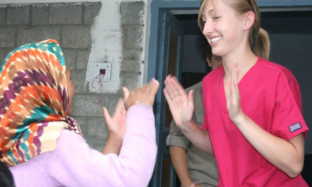 A young Himalayan girl plays a hand-clapping game with a young white woman in scrubs.