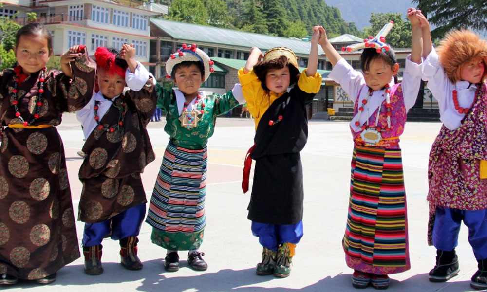 Six Tibetan children hold their linked hands high, wearing traditional regalia/dress.