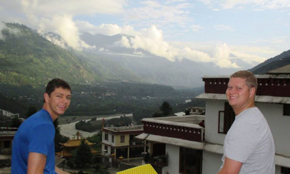 Two white, male students sit opposite side of the frame, the city and mountains stretched out behind them.