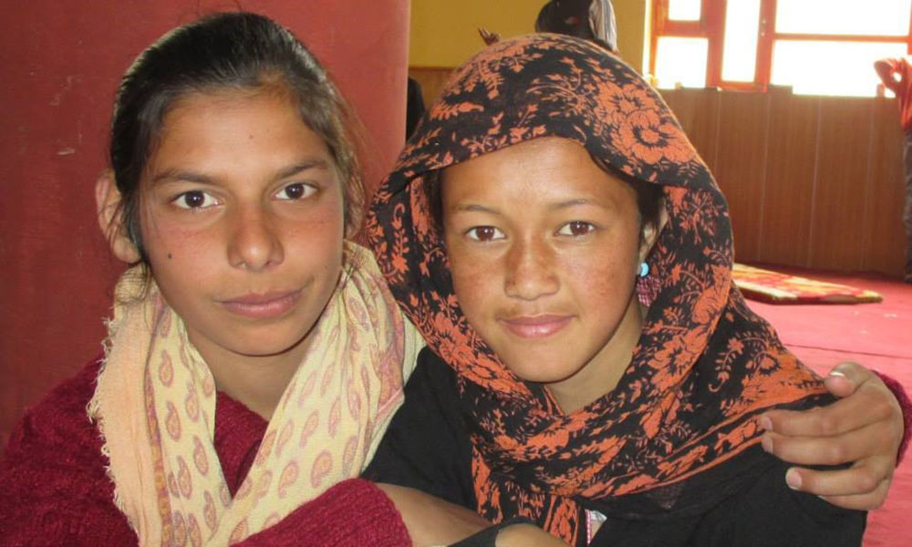 Two local girls in (head)scarves pose for a snapshot, staring directly into the camera.