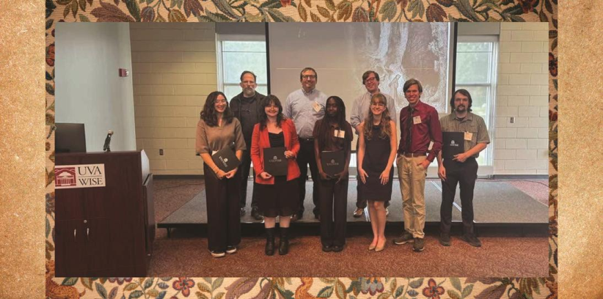 Attendees standing in front of a projector screen at the UVA Wise campus. Back row: Dr. Thomas Crofts, Dr. Josh Reid, Grant Bivens. Front row: Sydney Gnoth, Ruby Purgason, Suzi Peter, Rebekah Saulsbury, Zephaniah Wells, and Jordan Hoyos