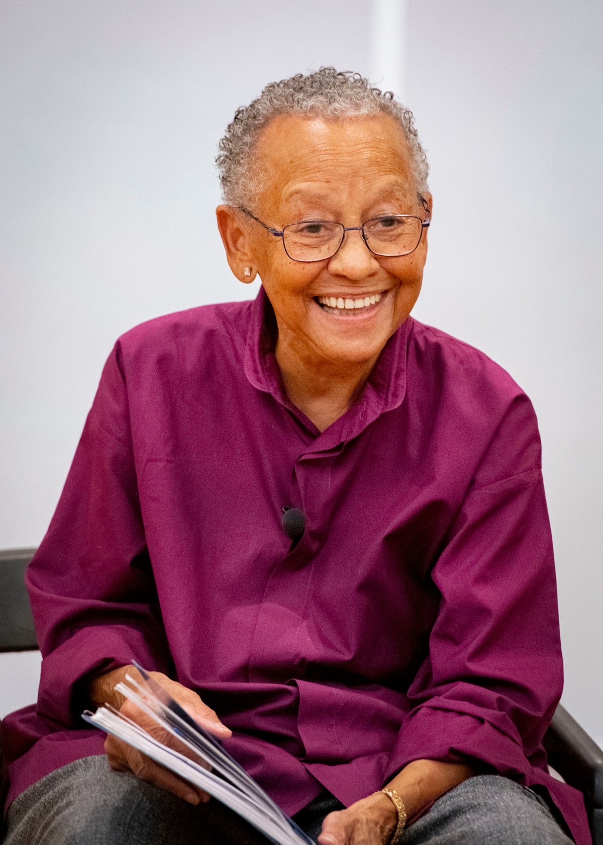 Nikki Giovanni sitting in a chair on stage smiling with a book in her lap
