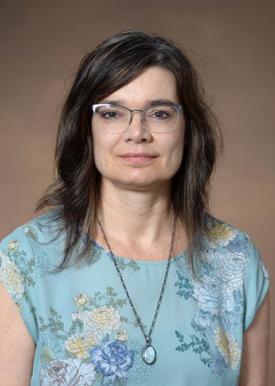 A woman with shoulder length, dark hair, in a floral top and glasses.