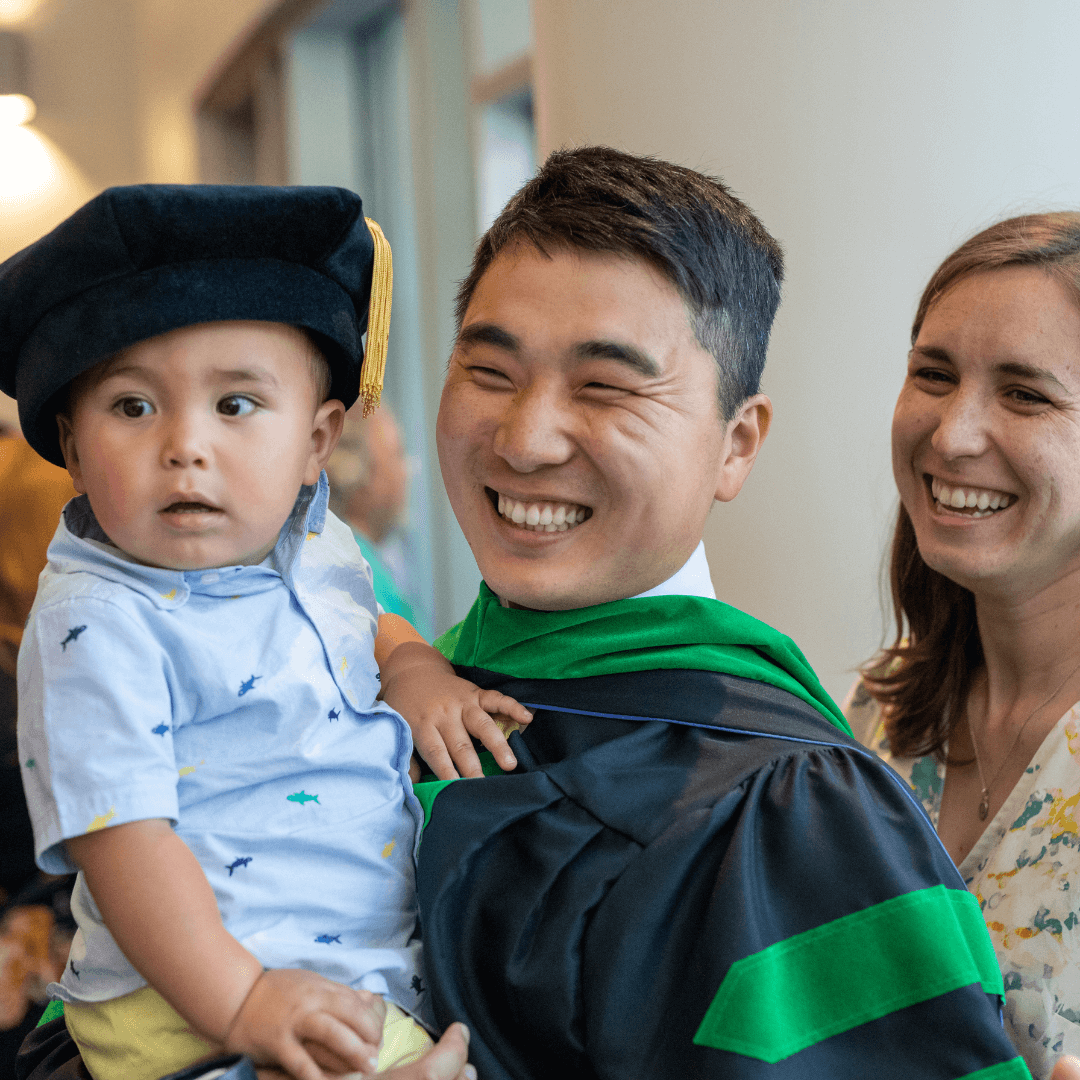 graduate holding his baby after putting his graduate cap on him