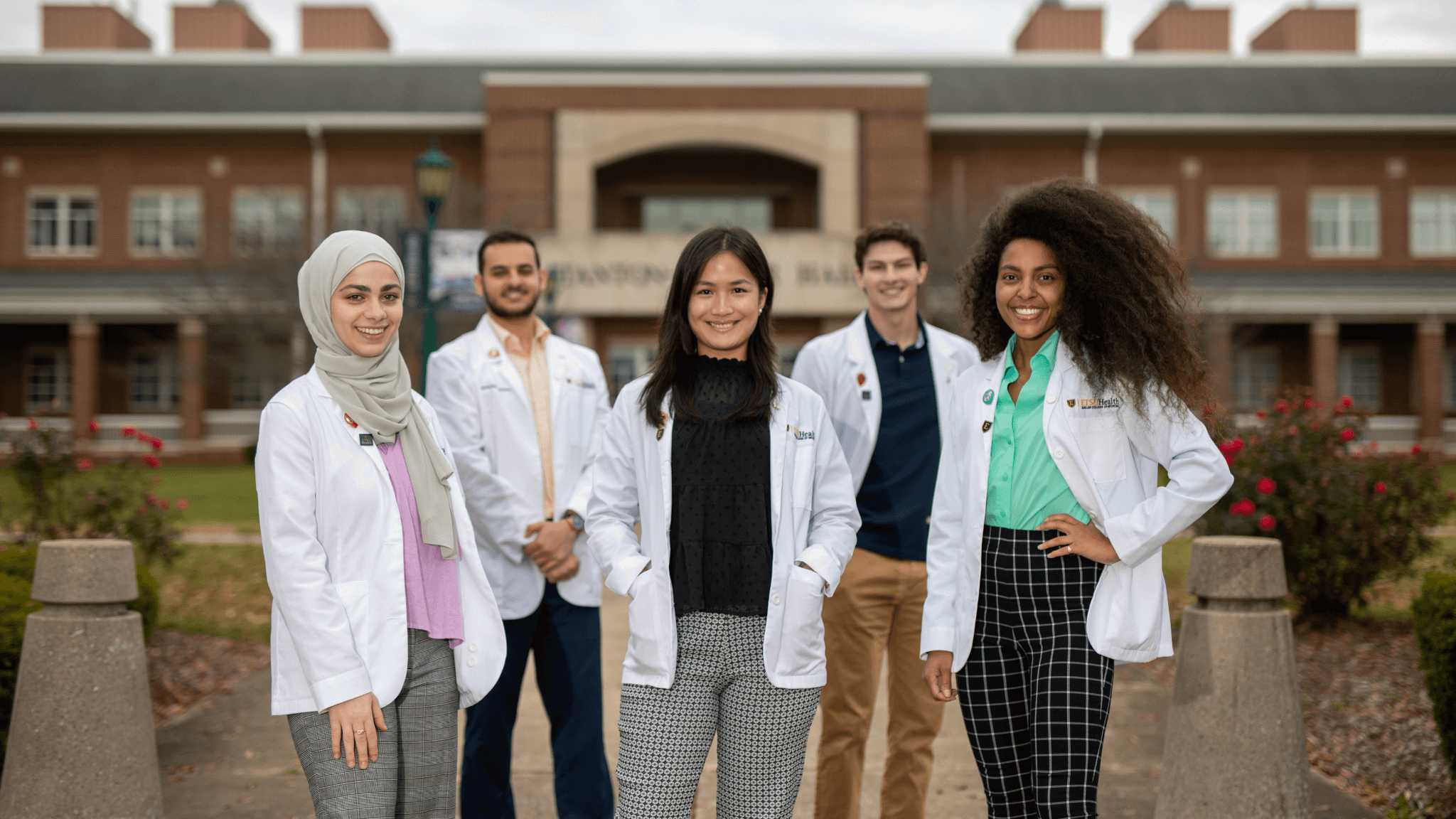 Five students standing in front of Stanton-Gerber Hall in their white coats.