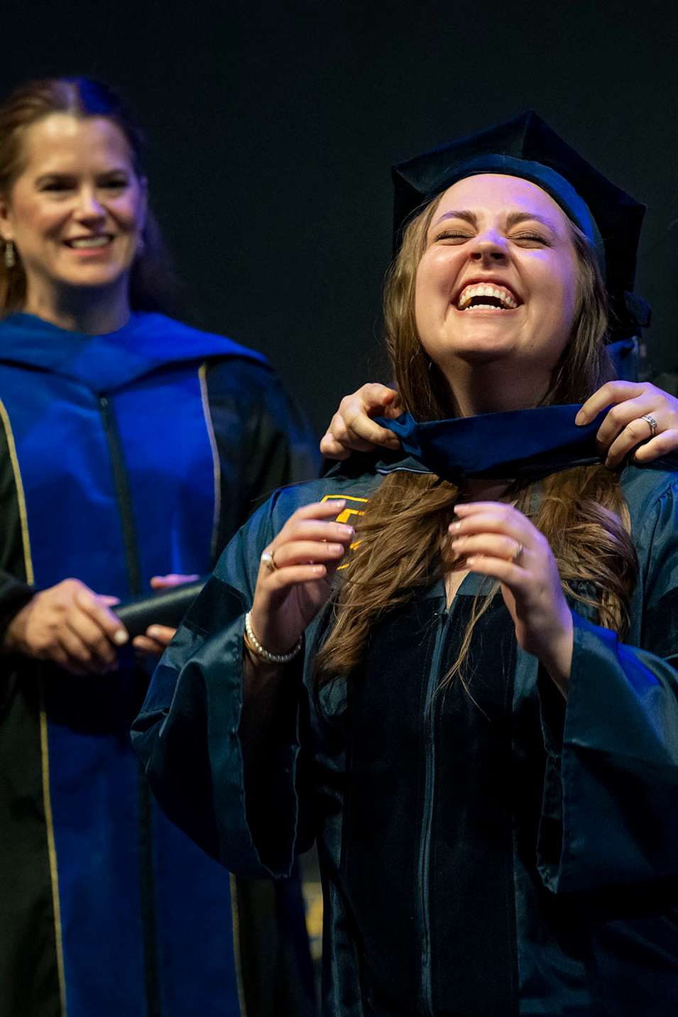 A graduate student laughs as her graduate hood is placed around her neck during the ETSU 2024 Spring Commencement ceremony