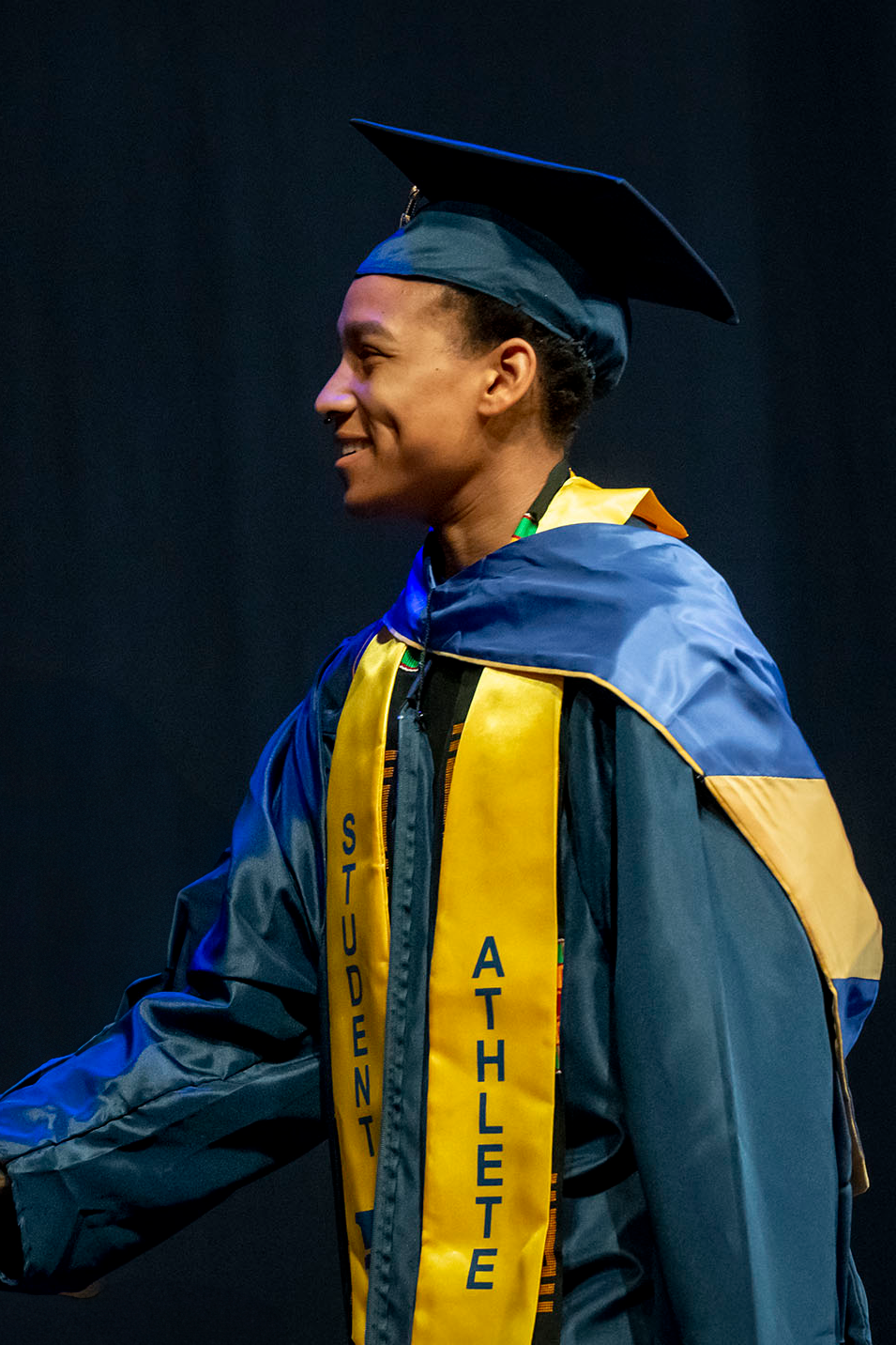 A smiling student wearing a student athlete stole crosses the stage during the 2024 ETSU Spring Commencement Ceremonye