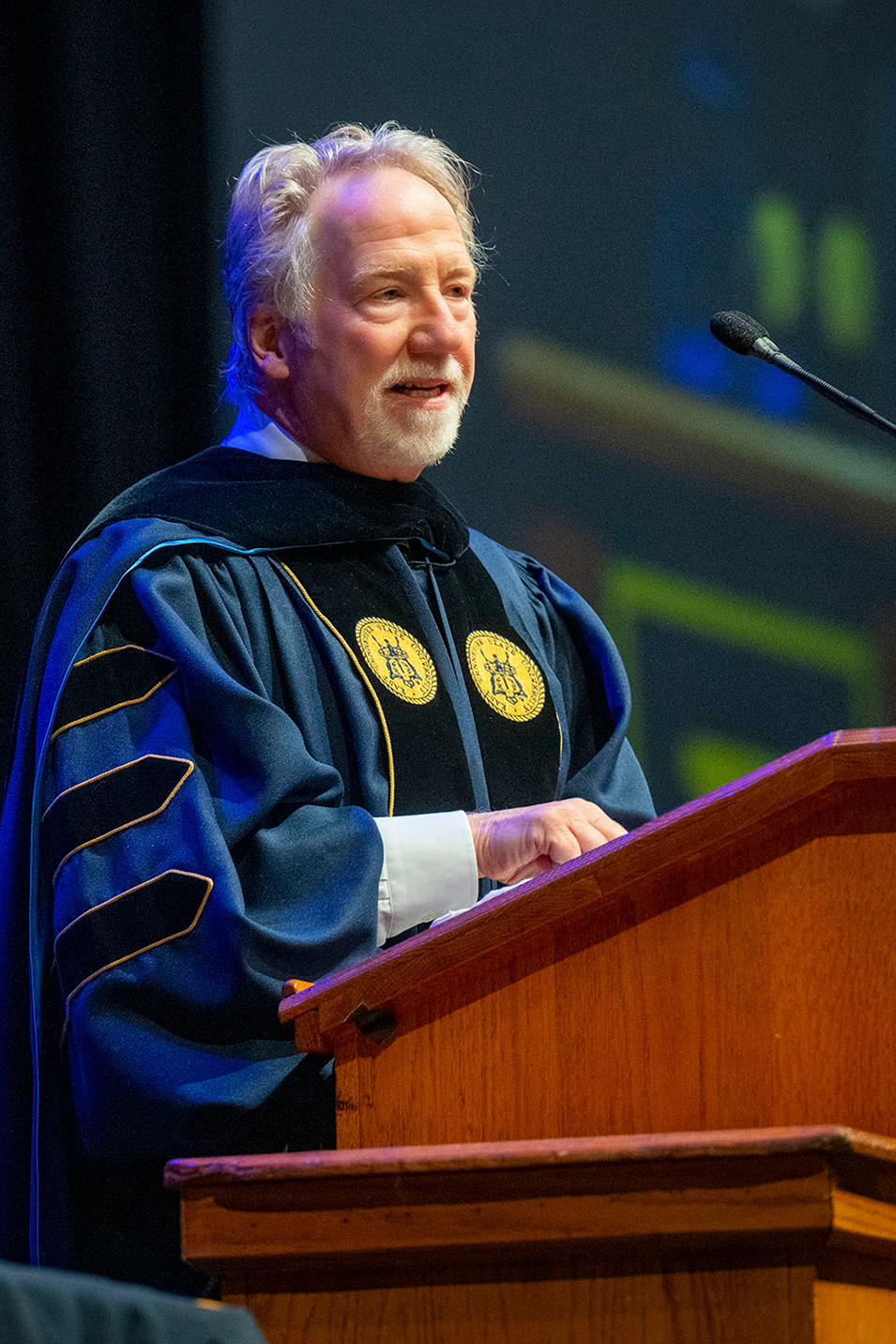 Actor and director Timothy Busfield stands at a podium delivering the keynote address at the ETSU 2024 Spring Commencement ceremony 