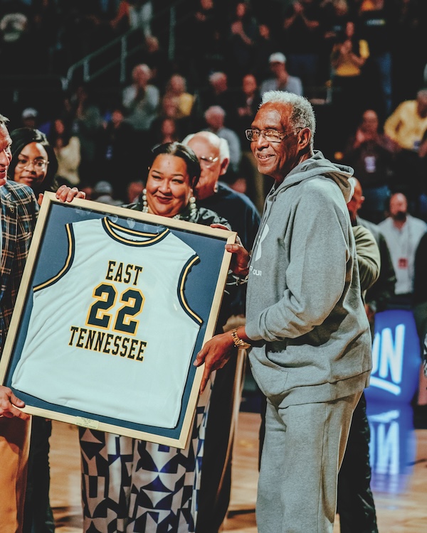 Tommy Woods stands with a female who is holding his framed, retired jersey that says East Tennessee 22.