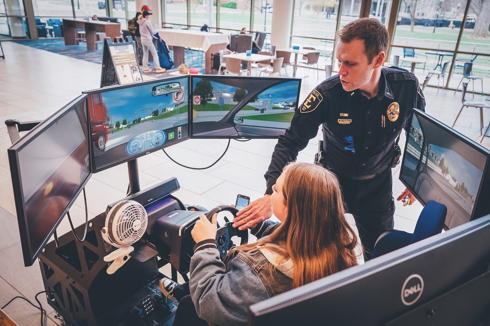 An ETSU police officer instructs a student, who is seated in the ETSU Distracted Driver Education Experience simulator.