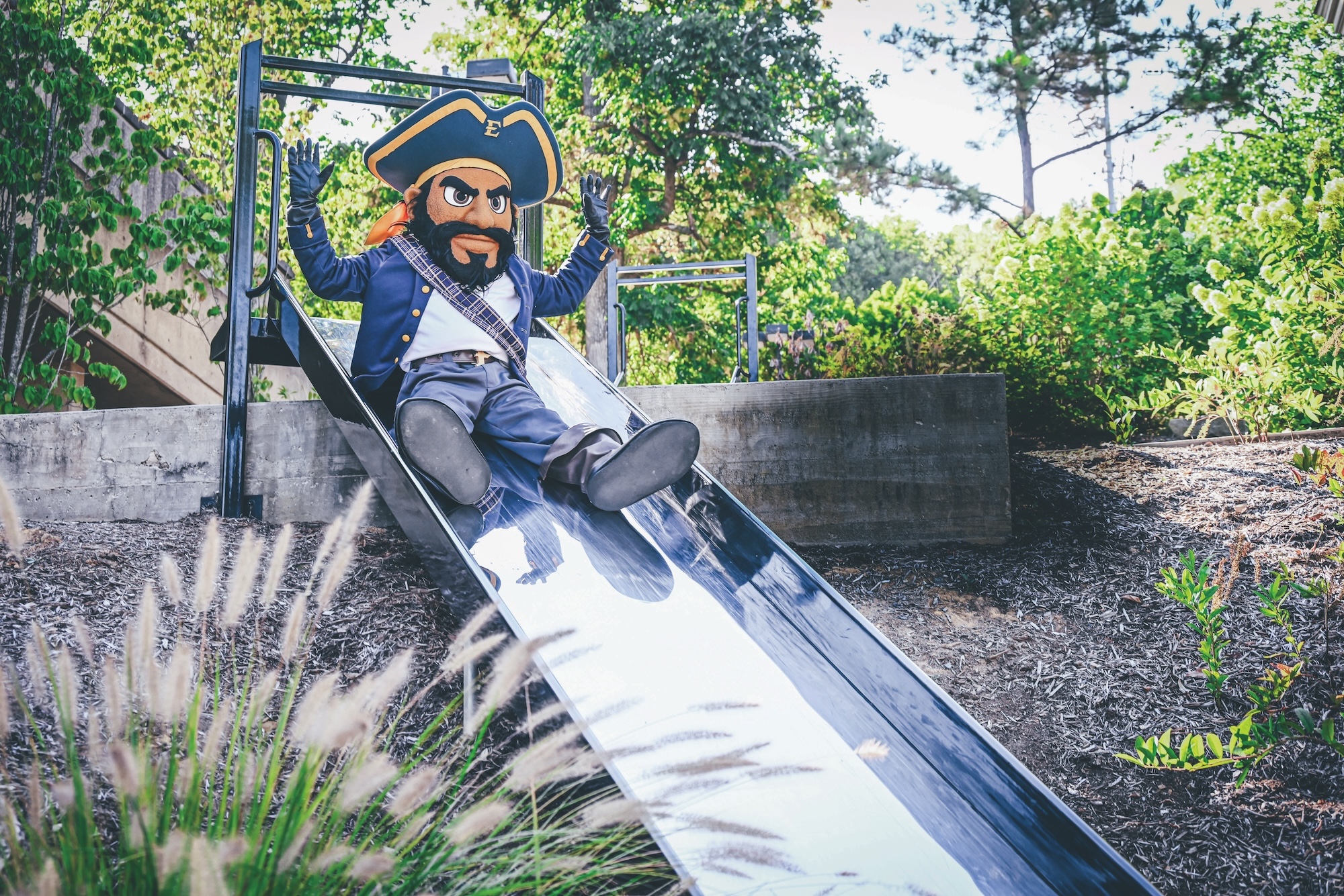 ETSU's mascot Bucky sliding down a metal slide in the University Commons on ETSU's campus