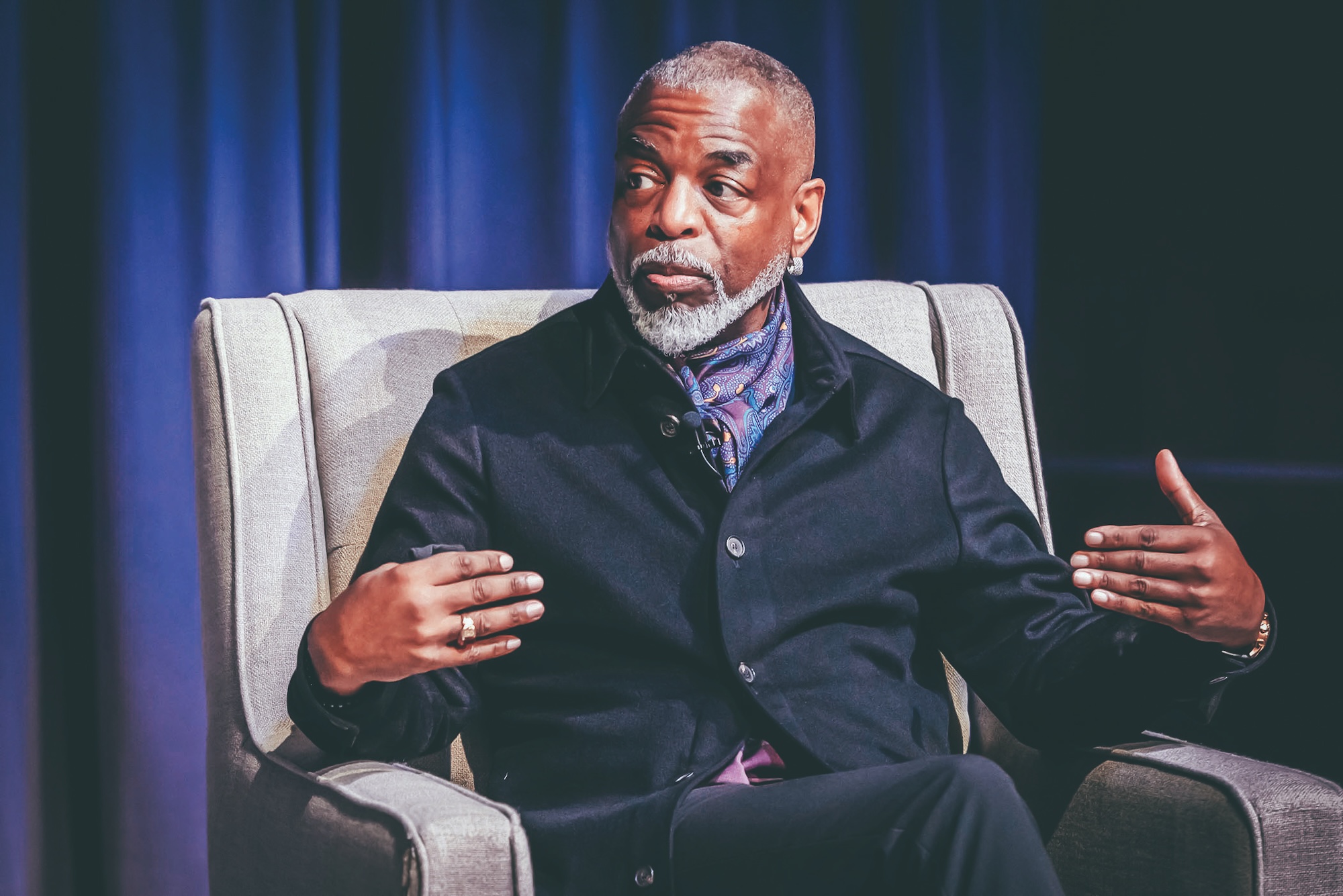 ETSU Festival of Ideas speaker LeVar Burton, seated in a chair, holds his arms out as he makes a point.