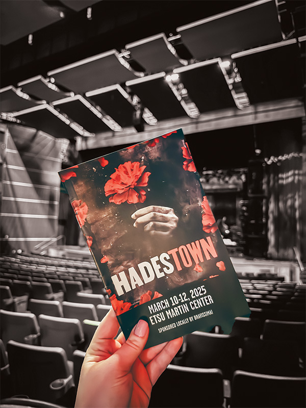 A hand holds the playbill for “Hadestown,” with the Martin Center stage in the background