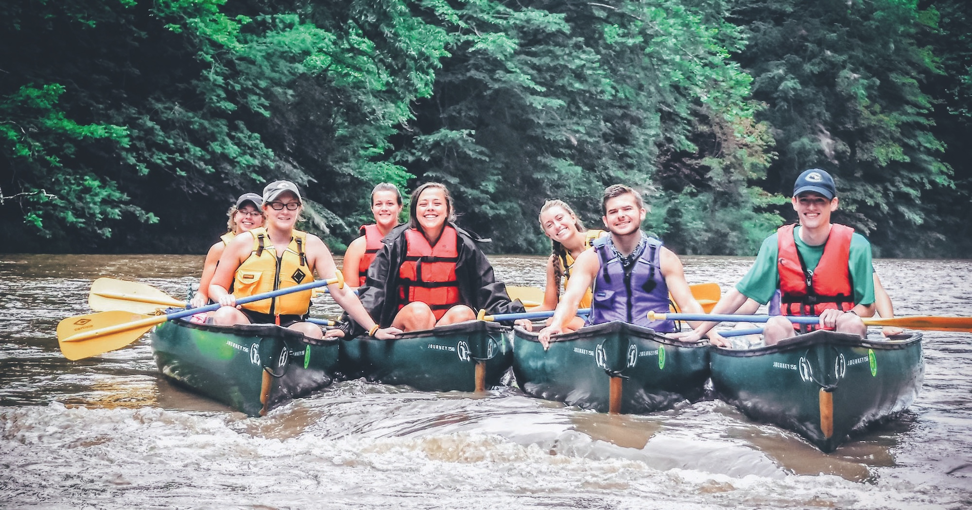 7 Roan Scholars smile at the camera while kayaking on a lake