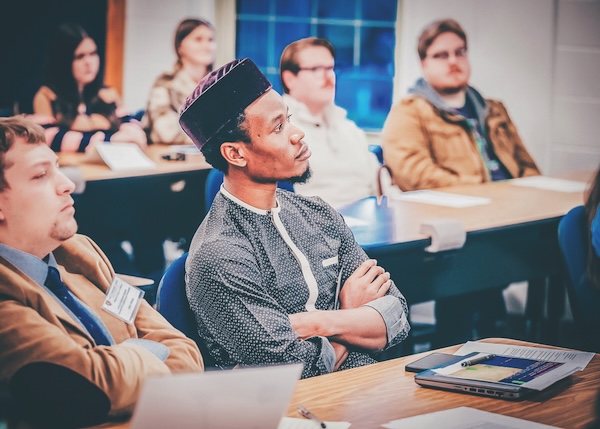 People with their arms crossed, seating at desks and listening.