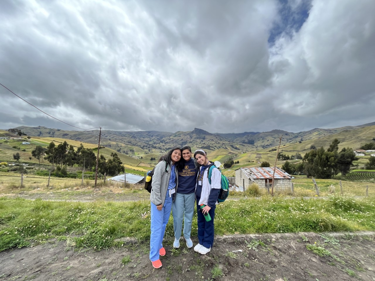 Three women standing in front of a beautiful hilly landscape with clouds