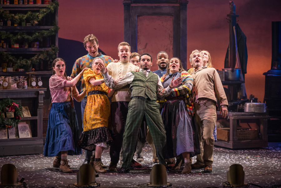 Stage photo from Dolly Parton's Smoky Mountain Christmas Carol showing ensemble cast members in period attire reacting with surprised expressions as snow falls on stage.
