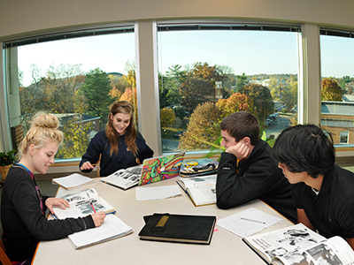 Students look over archival materials at a table in front of the Archives' large window overlooking campus.