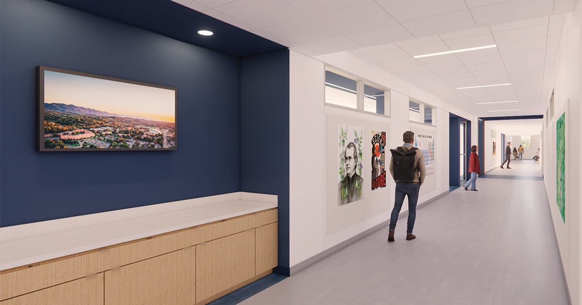 Rendering of an interior hallway in the renovated Brown Hall at ETSU with navy and white walls, framed student artwork, and a landscape photo of campus. A student walks down the corridor while others are visible farther ahead near classroom entrances.