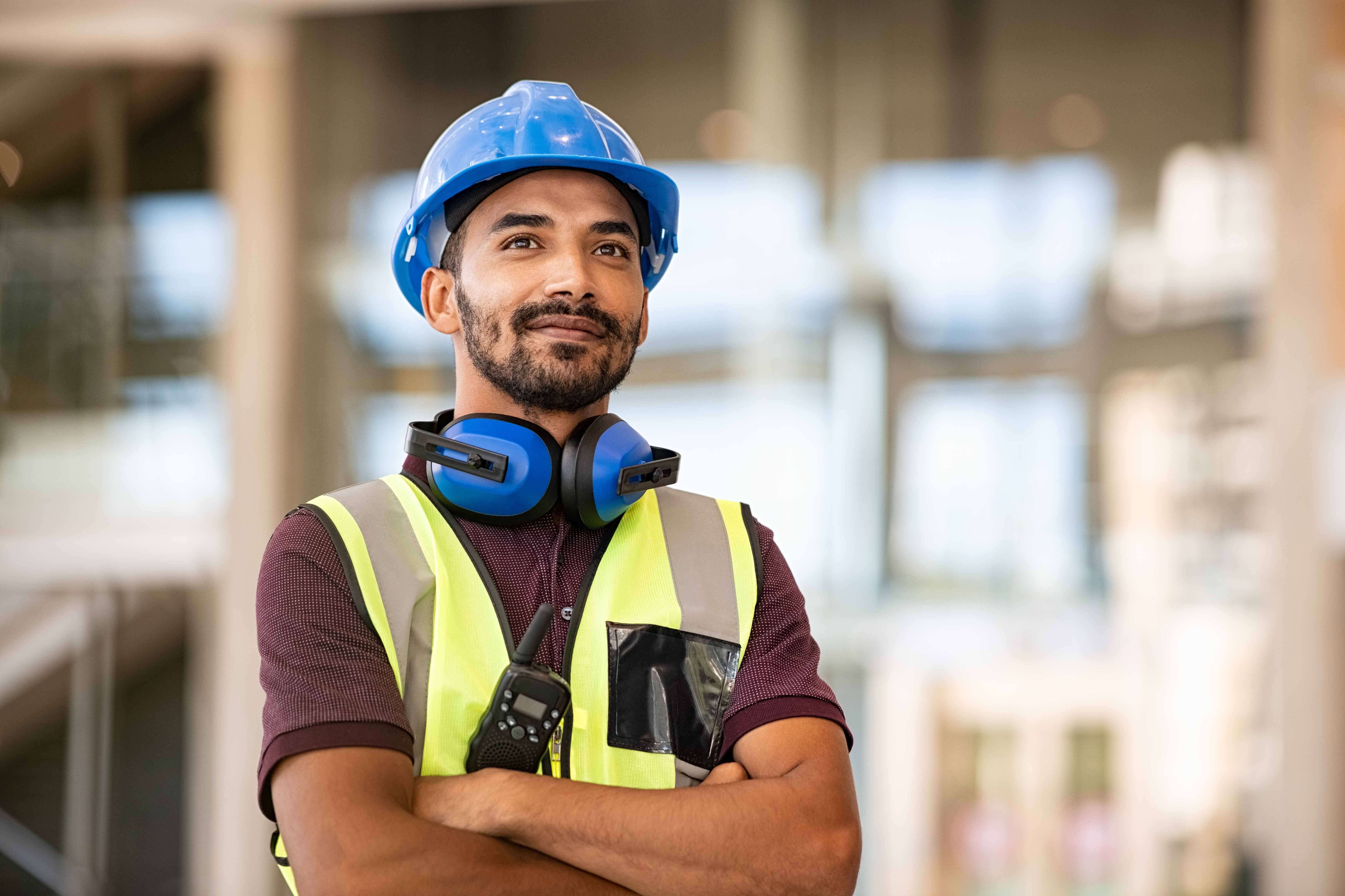 A man smiles and crosses his arms. He is wearing construction gear that implies he is the supervisor.