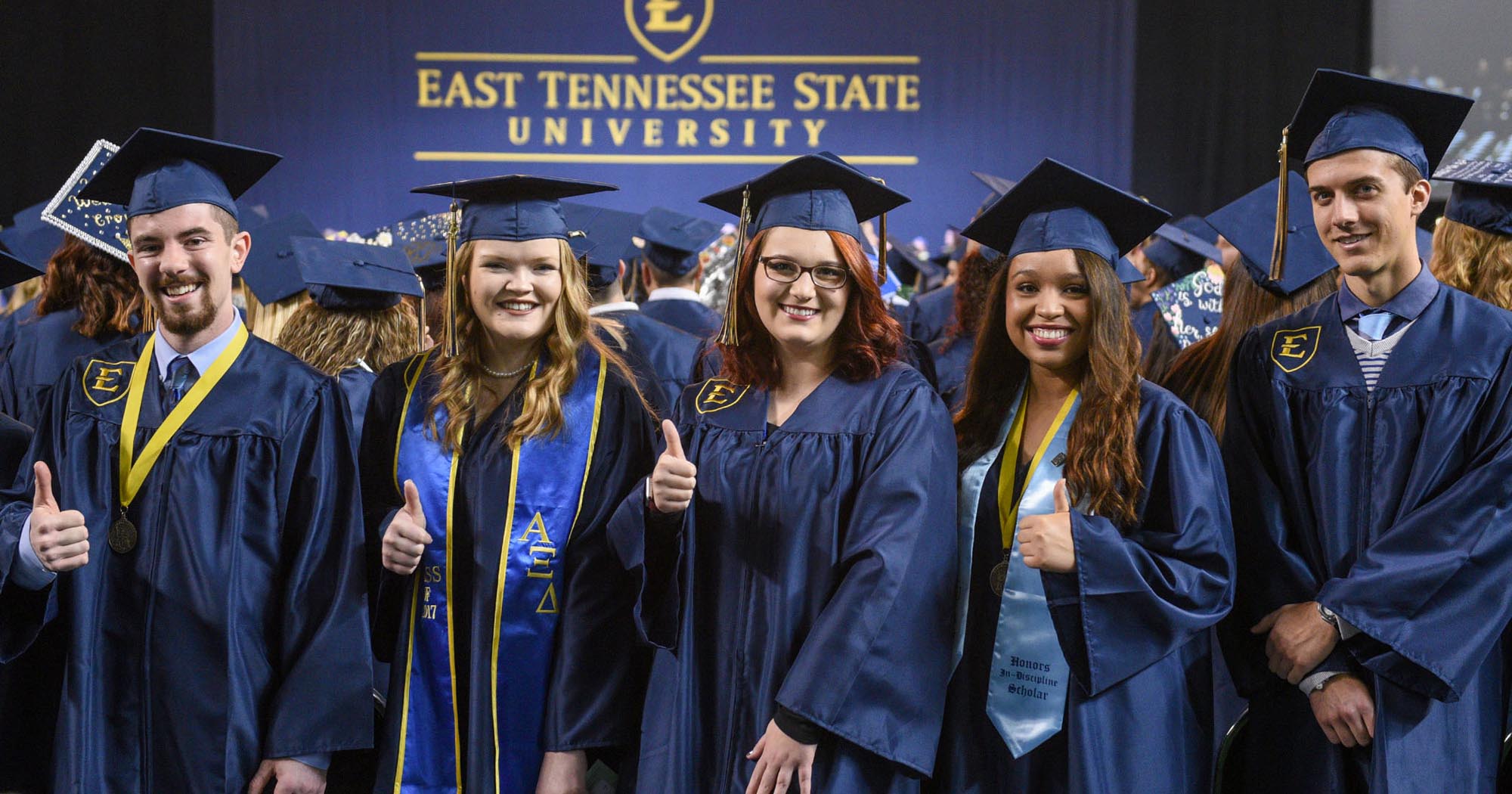 a group of graduate smile and gives a thumbs-up at graduation.