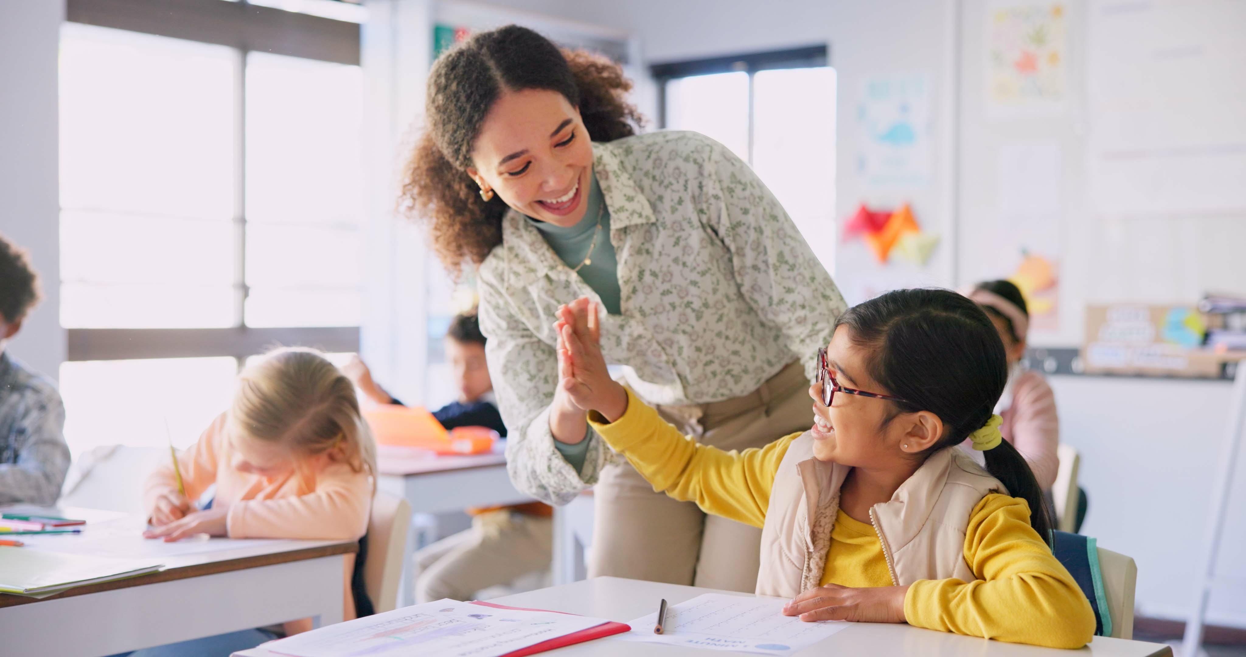 a young teacher high fives a young girl in a classroom.