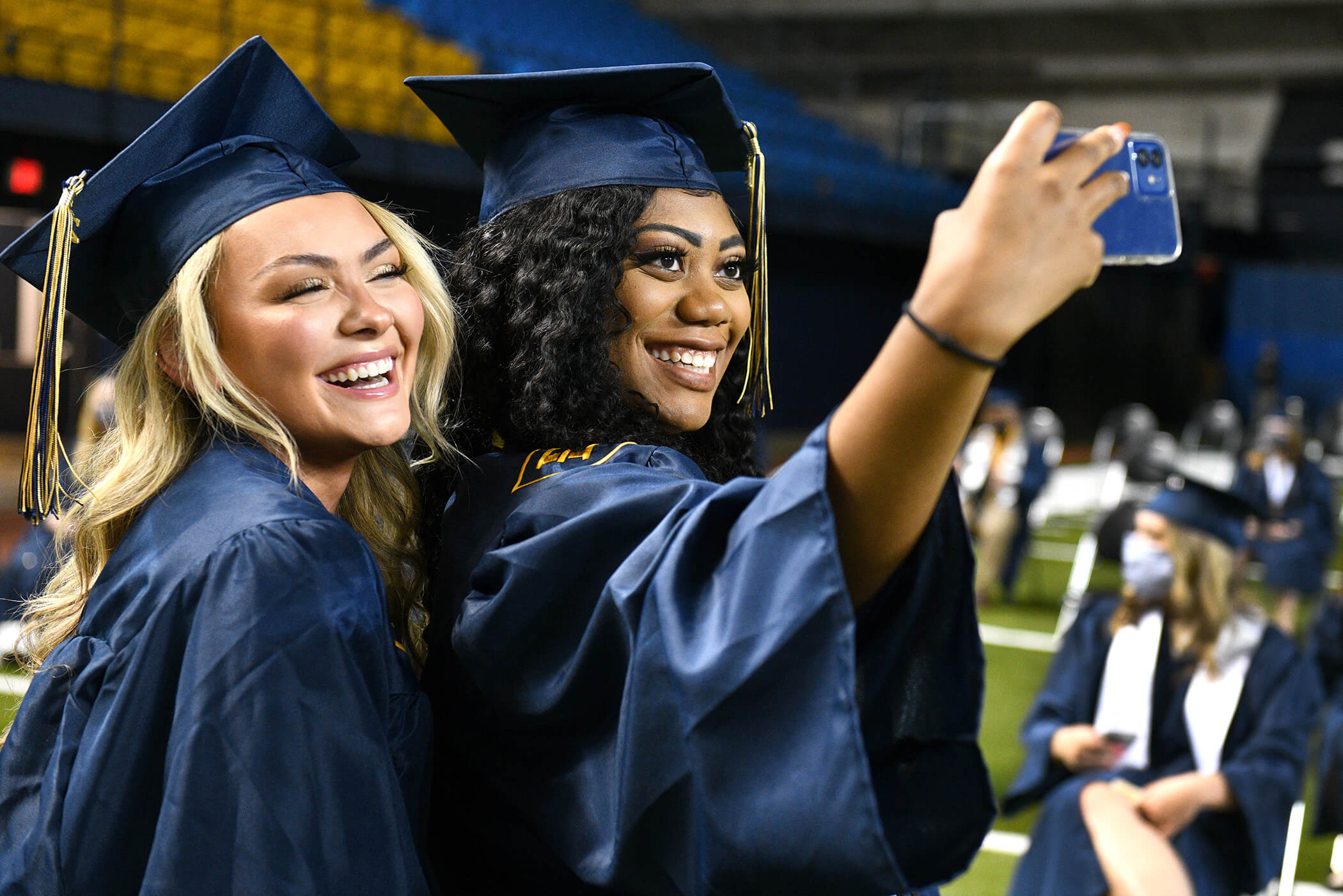 Two women take a smiling selfie at graduation. They are in their cap and gowns.