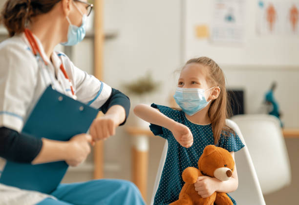 A young girl bumps elbows with a masked child life specialist. 