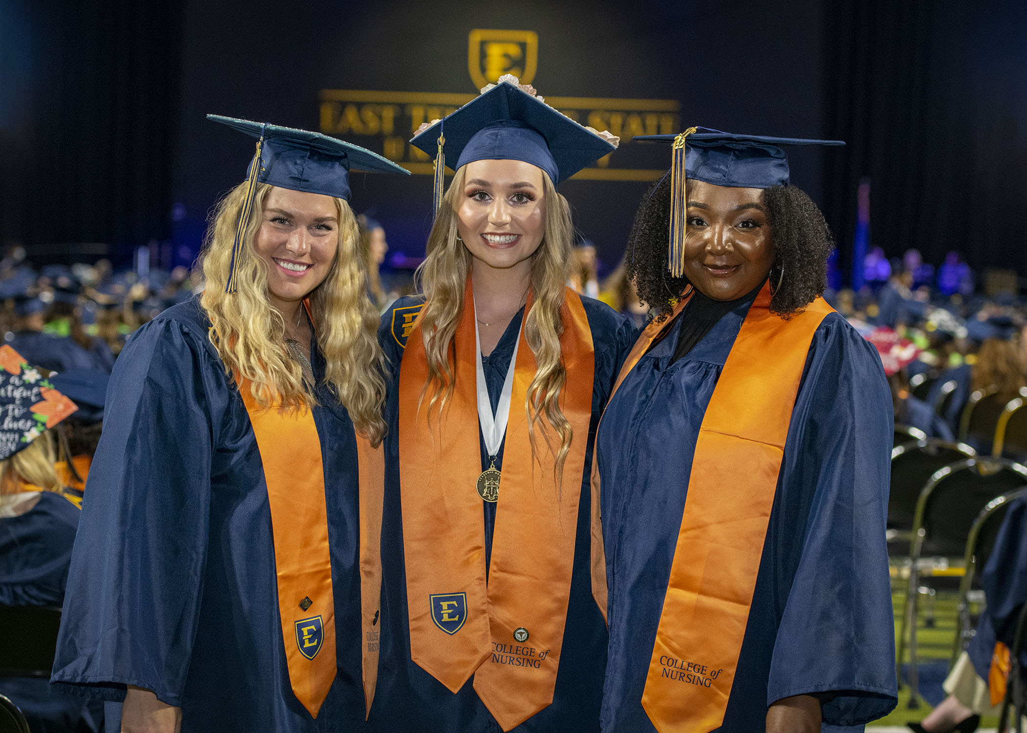 three women smile at graduation. They are wearing their cap and gowns. 