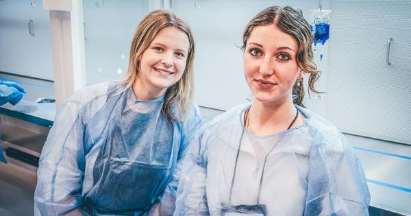 Two high school students at the Gatton Pharmacy summer camp. They are wearing scrubs and smiling at the camera with their heads close together.